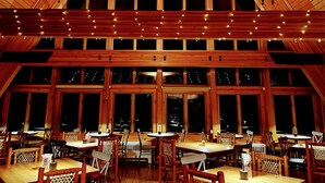A spacious dining area with multiple tables and chairs, large windows, and string lights. - NewVida Preserve (Jay)