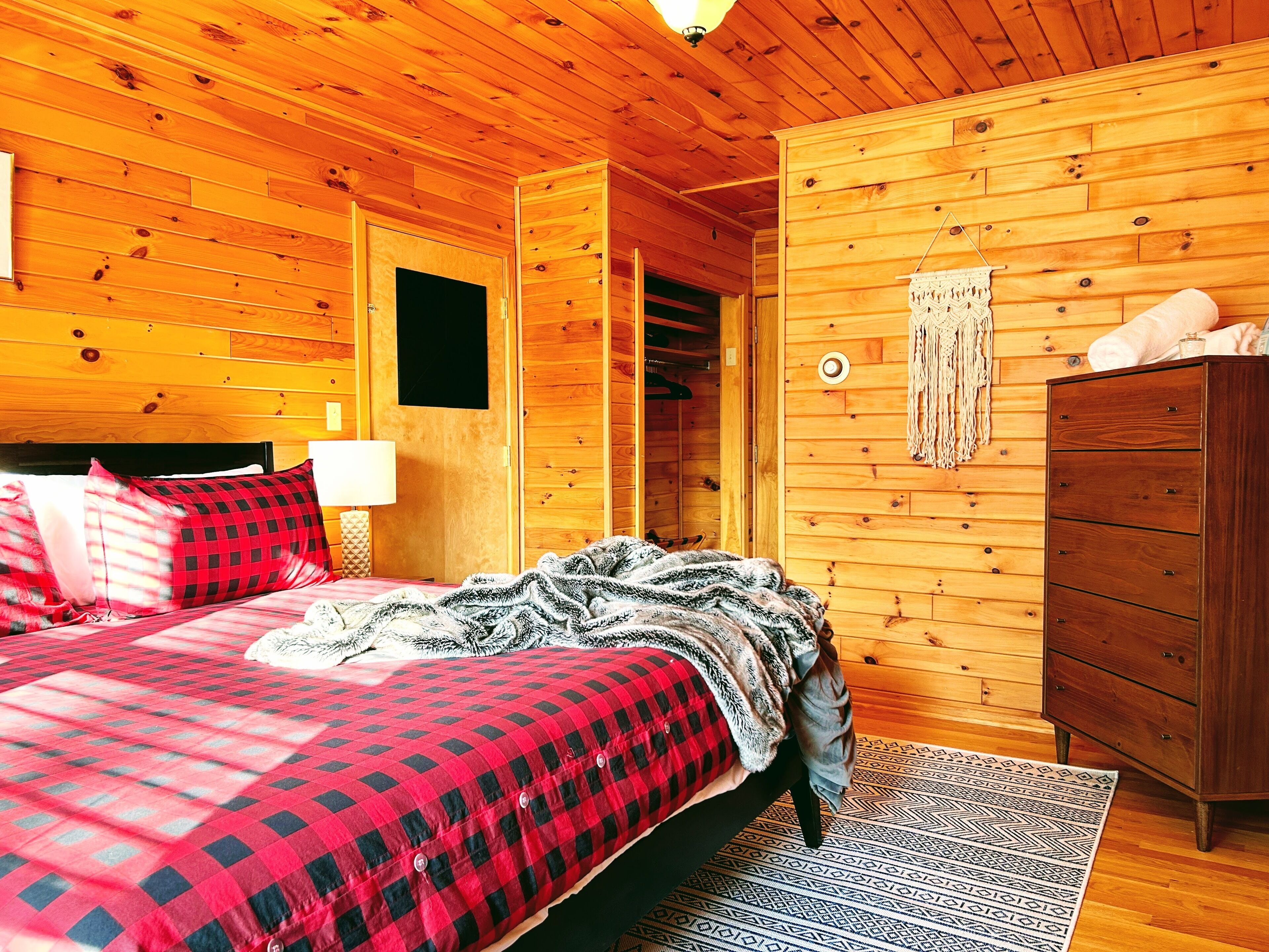 A wooden cabin bedroom with a bed, dresser, and a walk-in closet.