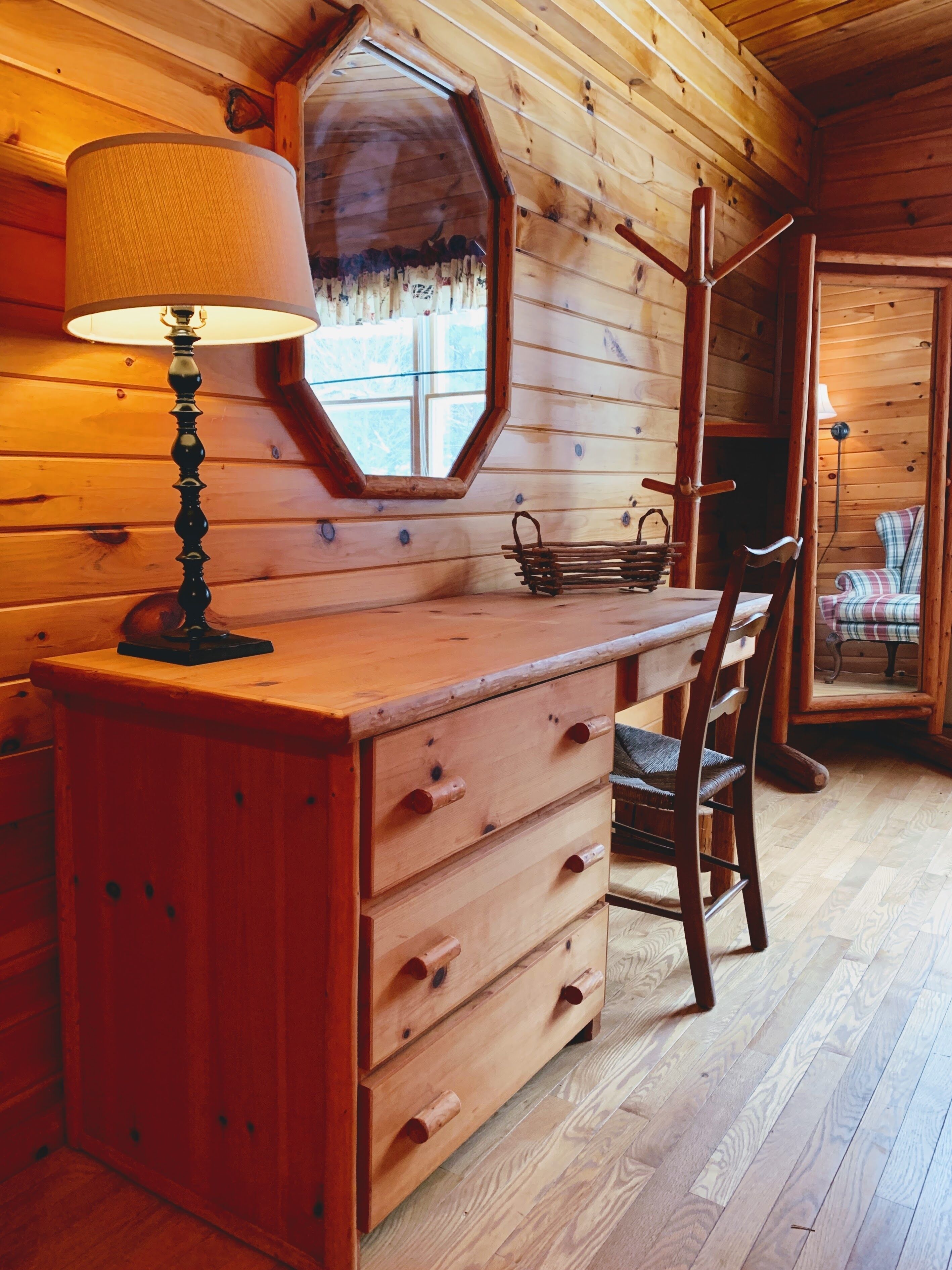 Interno di una baita in legno con una scrivania, una sedia, una lampada e uno specchio.