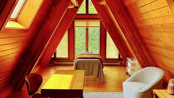 Un acogedor dormitorio en el ático con paredes de madera, un ventanal grande, una mesa de comedor, un sofá y una silla.
