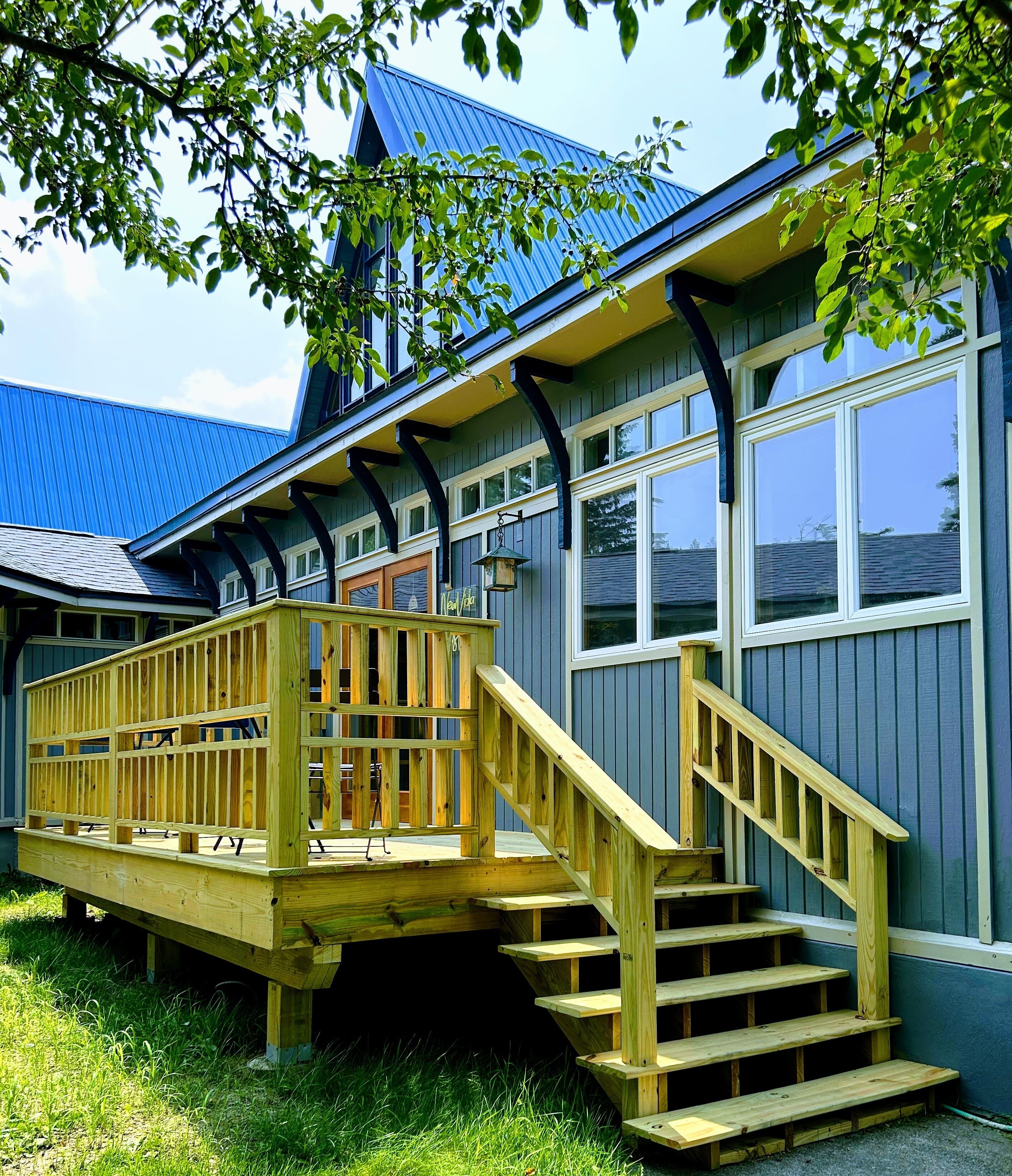 A wooden deck with a staircase leading to a building with a blue roof and white windows.