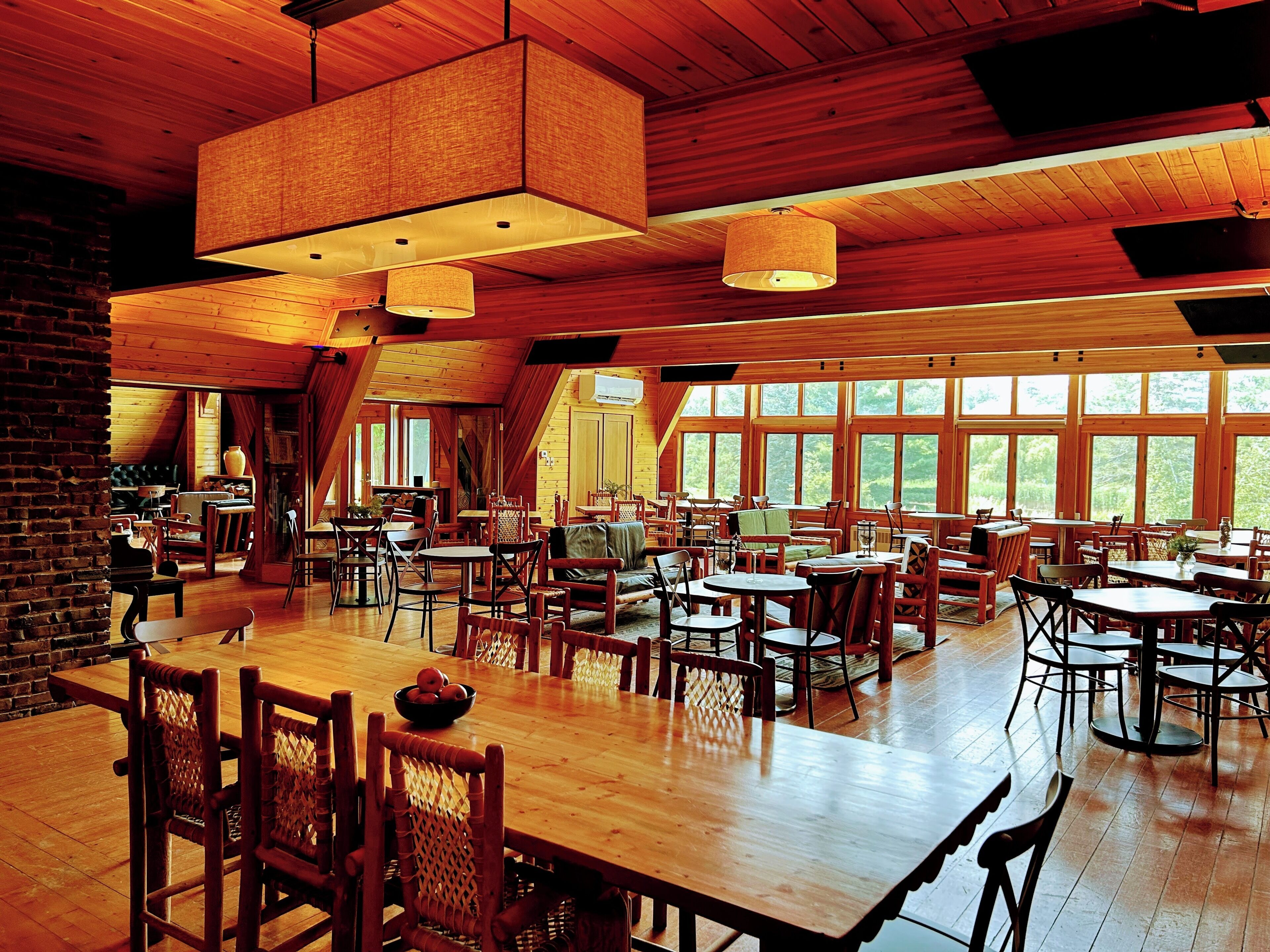 A spacious dining area with high ceilings and large windows, featuring wooden tables and chairs.