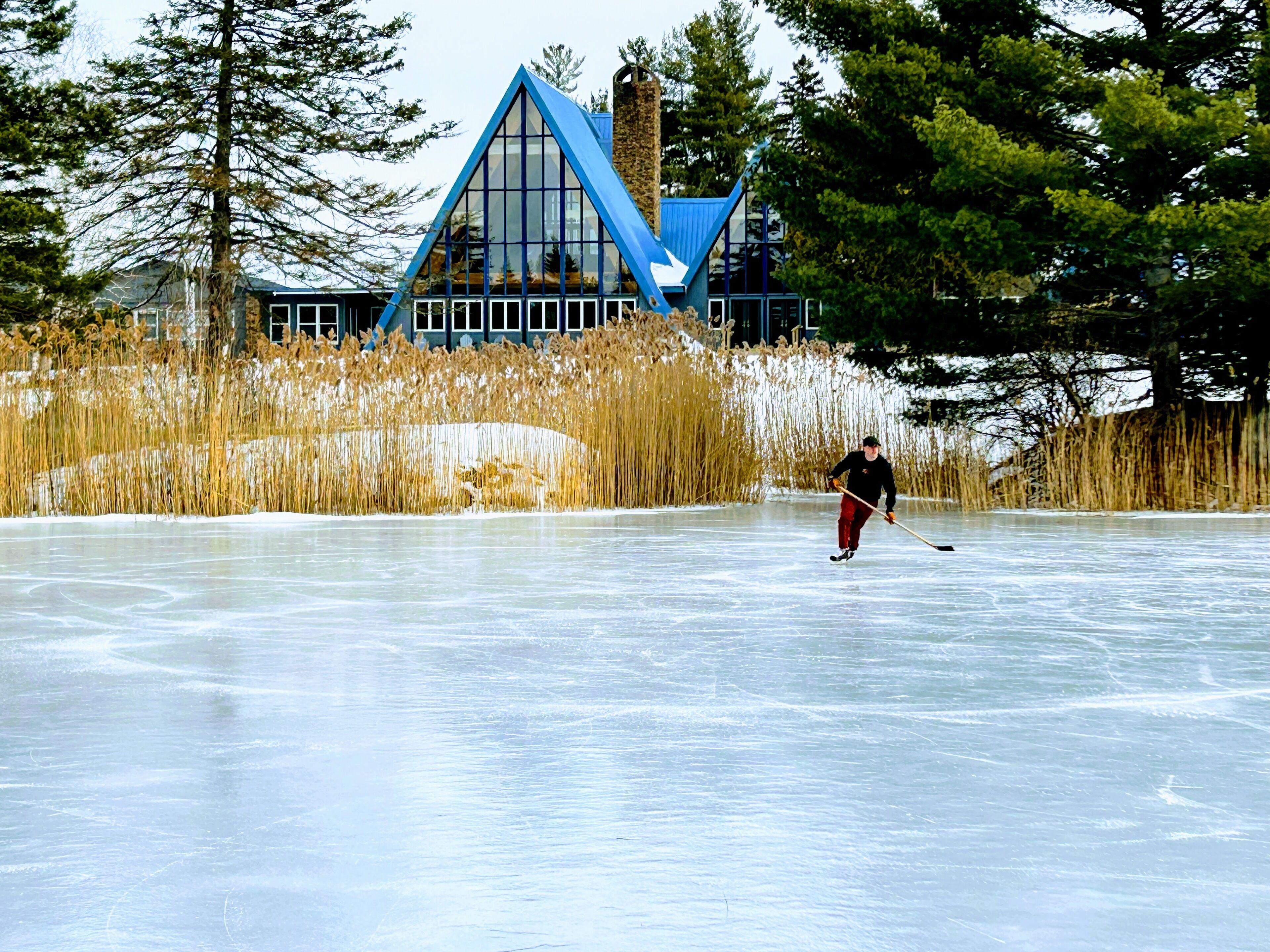 A person ice skating on a frozen lake with a house in the background.