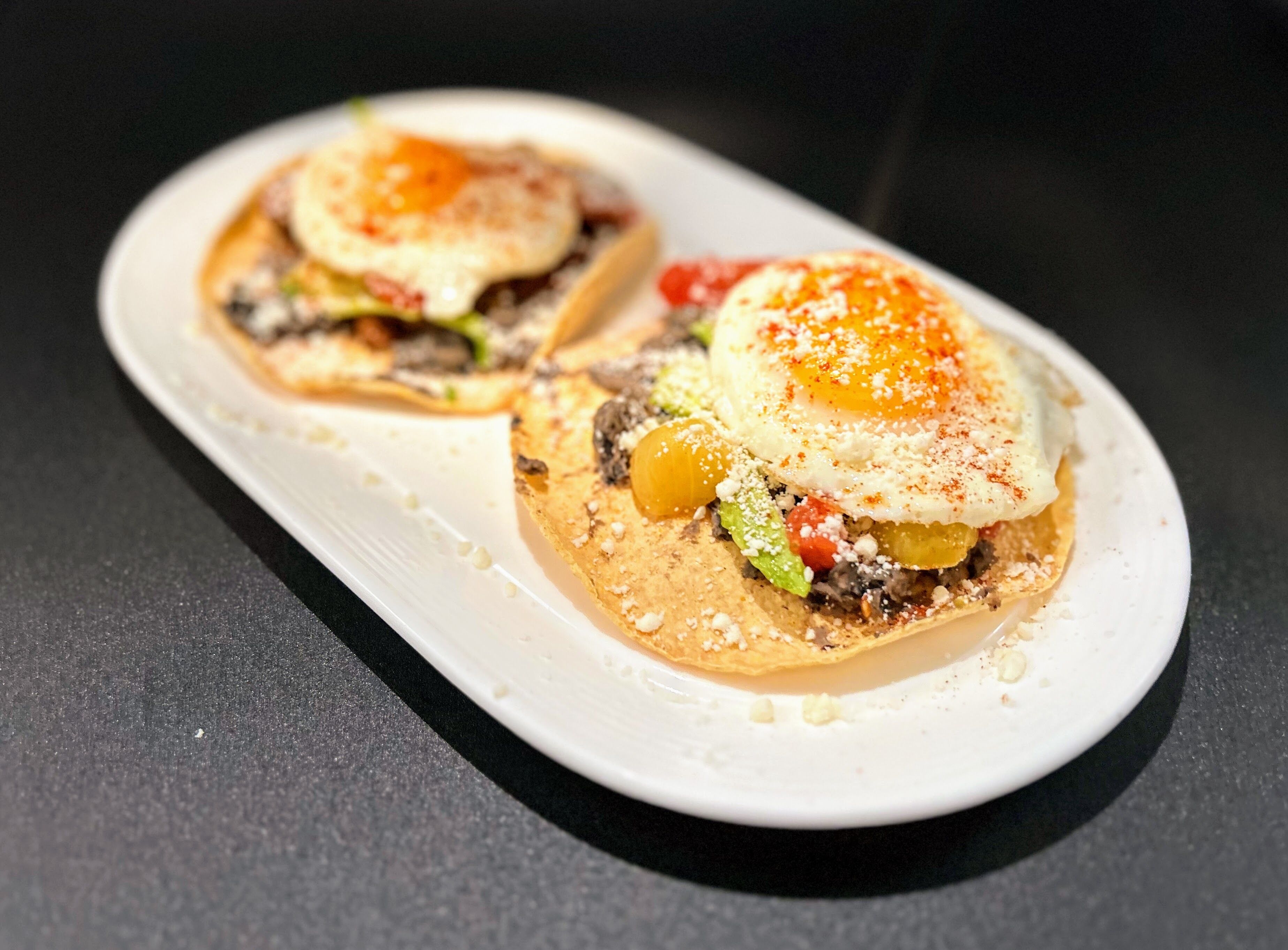 Twee taco's op een wit bord met een zwarte achtergrond.