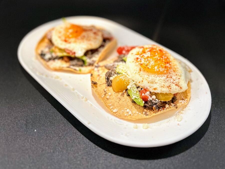Twee taco's op een wit bord met een zwarte achtergrond.