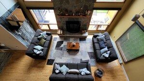 A spacious living area with a stone fireplace, two sofas, a coffee table, and a view of the outdoors through large windows.