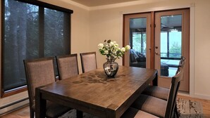 A dining room with a wooden table, six chairs, a vase with flowers, and a view through a glass door.