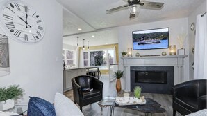 Un salon moderne avec une cheminée, une grande horloge murale et un téléviseur diffusant un paysage pittoresque.