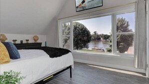 Une chambre avec une grande fenêtre, un lit, une télévision et une vue sur une rivière et des arbres.