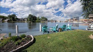 Une jetée au bord du lac, avec des chaises Adirondack vertes et une zone herbeuse.
