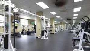 Un gimnasio con diversas máquinas de ejercicio, un espejo grande y un techo con luces fluorescentes.