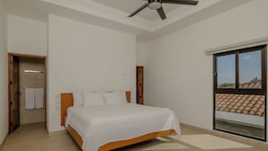 Een slaapkamer met een bed, een plafondventilator, een schuifdeur naar een balkon en een houten deur naar een badkamer.