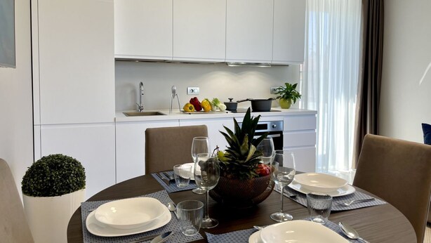 A modern dining area with a round table set for four, a kitchen in the background, and a potted plant on the left. - Beautiful flat on the second floor with lift with beautiful modern fittings and large windows with a splendid view of the Viareggio dock just a few minutes' walk from the promenadeand beach.Elegantly furnished it consists of a living room with modern wal (Viareggio)