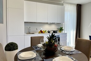 A modern dining area with a round table set for four, a kitchen in the background, and a potted plant on the left. - Beautiful flat on the second floor with lift with beautiful modern fittings and large windows with a splendid view of the Viareggio dock just a few minutes' walk from the promenadeand beach.Elegantly furnished it consists of a living room with modern wal (Viareggio)