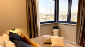 A hotel room with a bed, a lamp, a potted plant, and a view of a harbor through a window. - Beautiful flat on the second floor with lift with beautiful modern fittings and large windows with a splendid view of the Viareggio dock just a few minutes' walk from the promenadeand beach.Elegantly furnished it consists of a living room with modern wal (Viareggio)