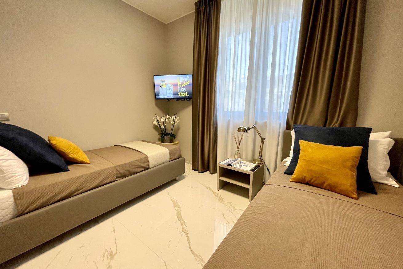 A modern hotel room with a sofa bed, a small table with a lamp, and a TV mounted on the wall.