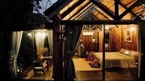 A cozy cabin with a glass door leading to a bedroom with a bed, a small table, and a chair. - Wilderness Treehouse Above a Stunning Waterfall (Tambon Pa Miang)