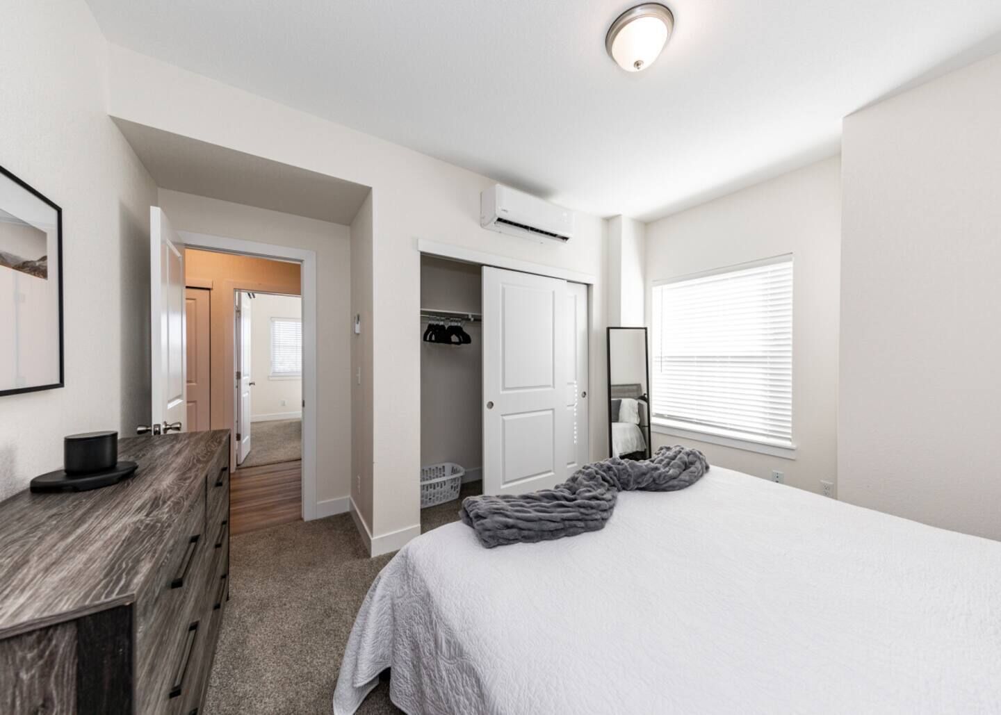 Een slaapkamer met een bed, een dressoir, een inloopkast en een raam met jaloezieën.
