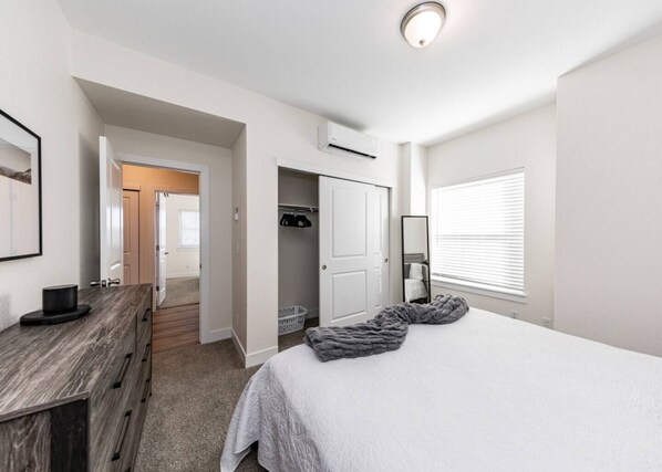Une chambre à coucher comprenant un lit, une commode, un dressing et une fenêtre avec des stores.