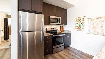 A modern kitchen with stainless steel appliances, dark cabinetry, and a wooden floor.