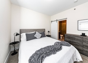 A modern bedroom with a bed, bedside lamps, a wooden headboard, a grey blanket, and a wooden dresser. - 2 Bed 2 Bath Near Garden of the Gods Near Nature (Colorado Springs)