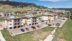 A residential area with multi-story apartment buildings, a parking lot, and a hilly landscape in the background.