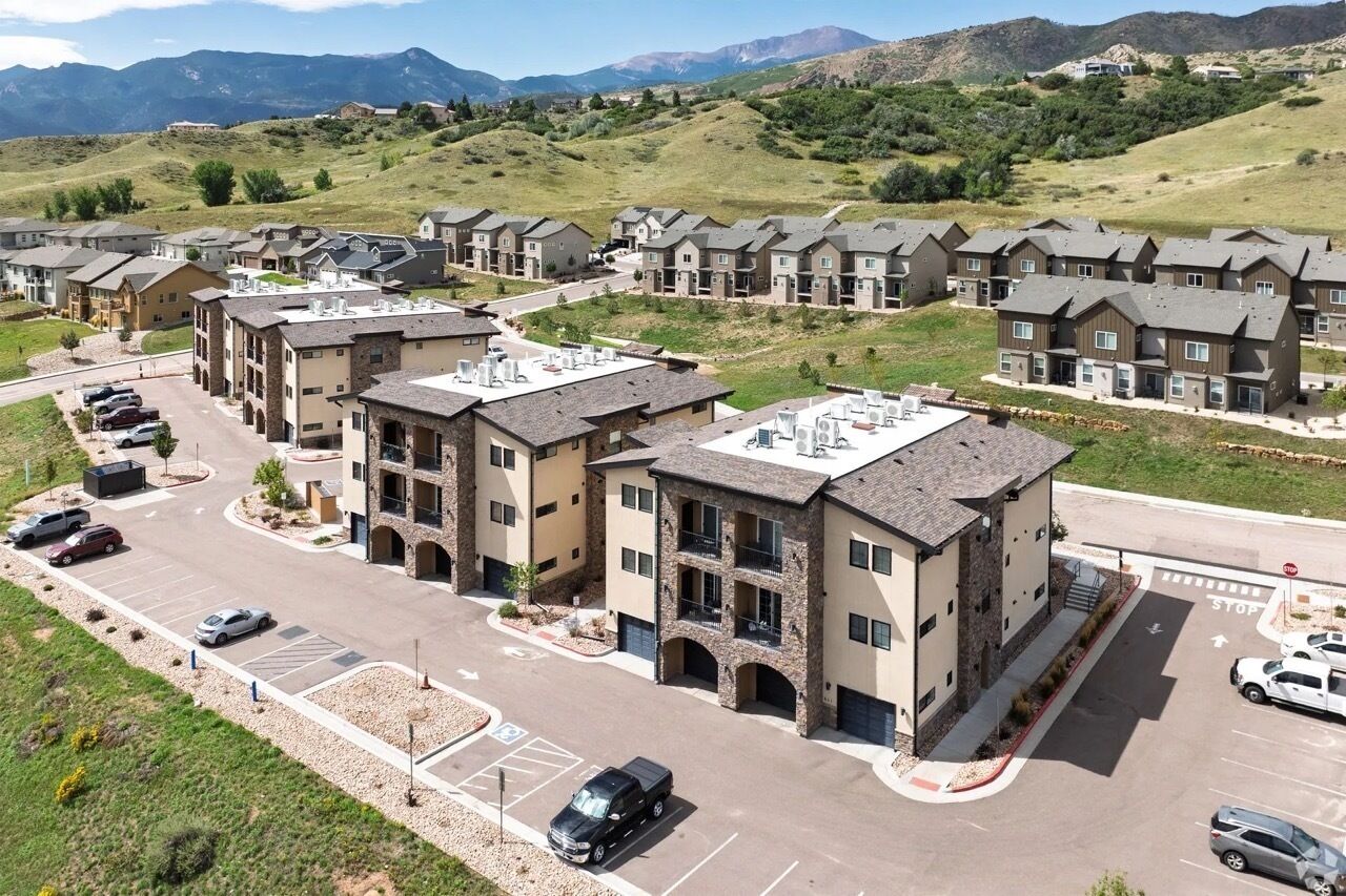 A residential area with multi-story buildings, a parking lot, and a mountainous backdrop.