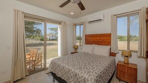 A bedroom with a large bed, a ceiling fan, and a view of the outdoors through a sliding glass door. - Casa de Amor B-58                                                             . (Villa El Carmen)