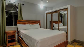 Quarto com cama de madeira, mesa de cabeceira, guarda-roupa e janela com cortinas.