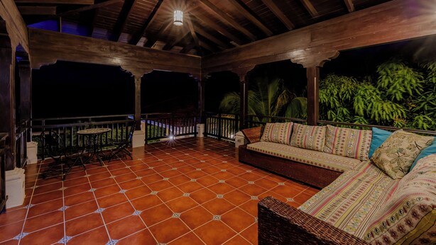 An outdoor covered patio with a tiled floor, wooden furniture, and a view of greenery. - Casa de Amor B-58                                                             . (Villa El Carmen)