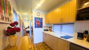 A modern kitchen with wooden cabinets, a sink, and a countertop. There is a vase with red roses on the left and a painting on the wall.