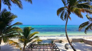 A beach view with palm trees, a wooden deck, and a sign for 'The Zanzibar Beach House'.