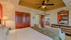 Une chambre à coucher avec un grand lit, des portes en bois, un ventilateur de plafond et une commode avec un miroir.