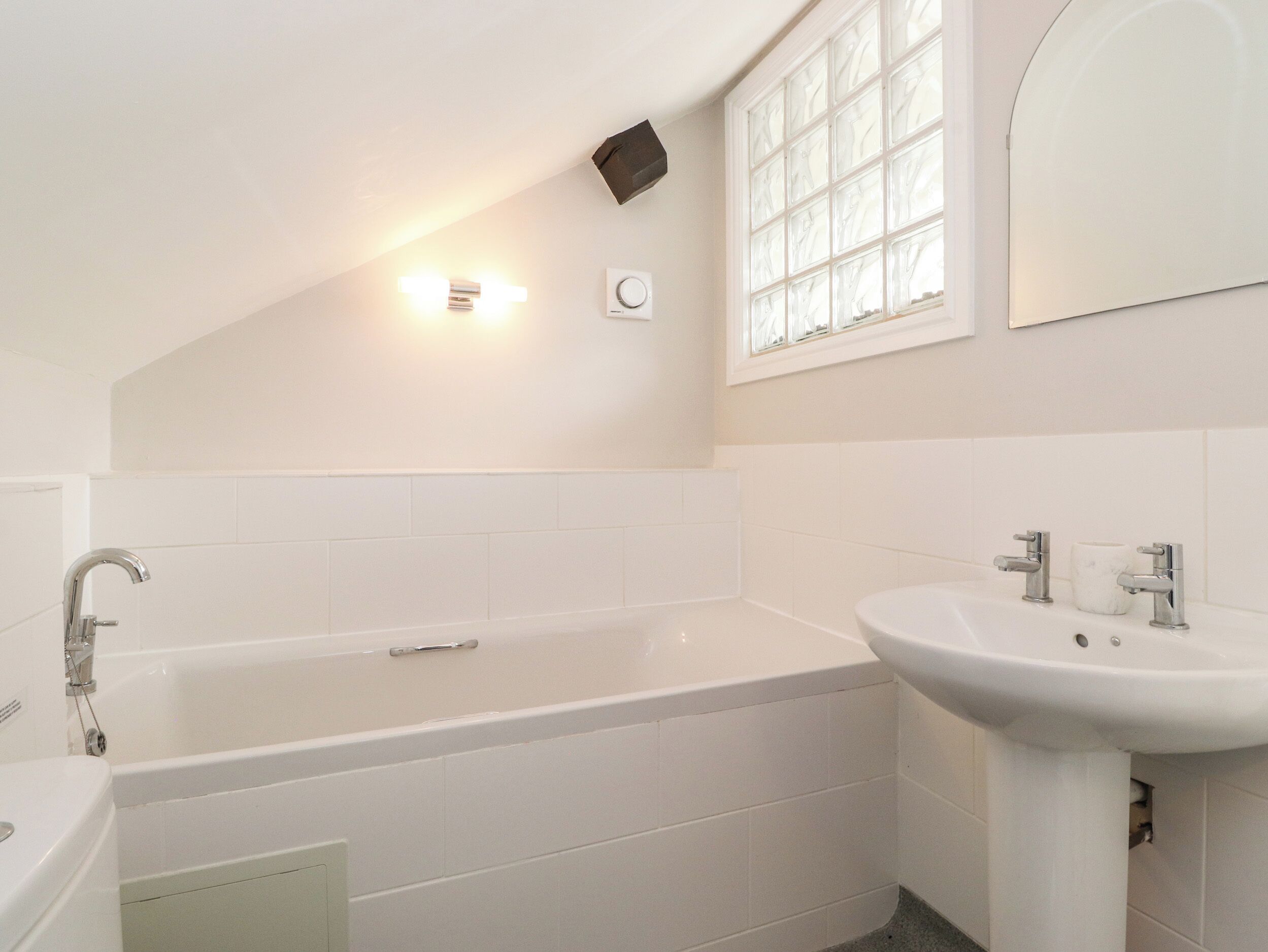 A modern bathroom with a freestanding bathtub, a pedestal sink, and a window with frosted glass.
