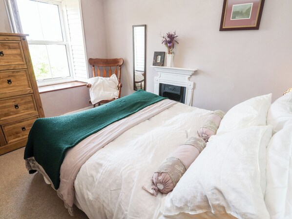 Een slaapkamer met een bed, dressoir, stoel, open haard en raam.