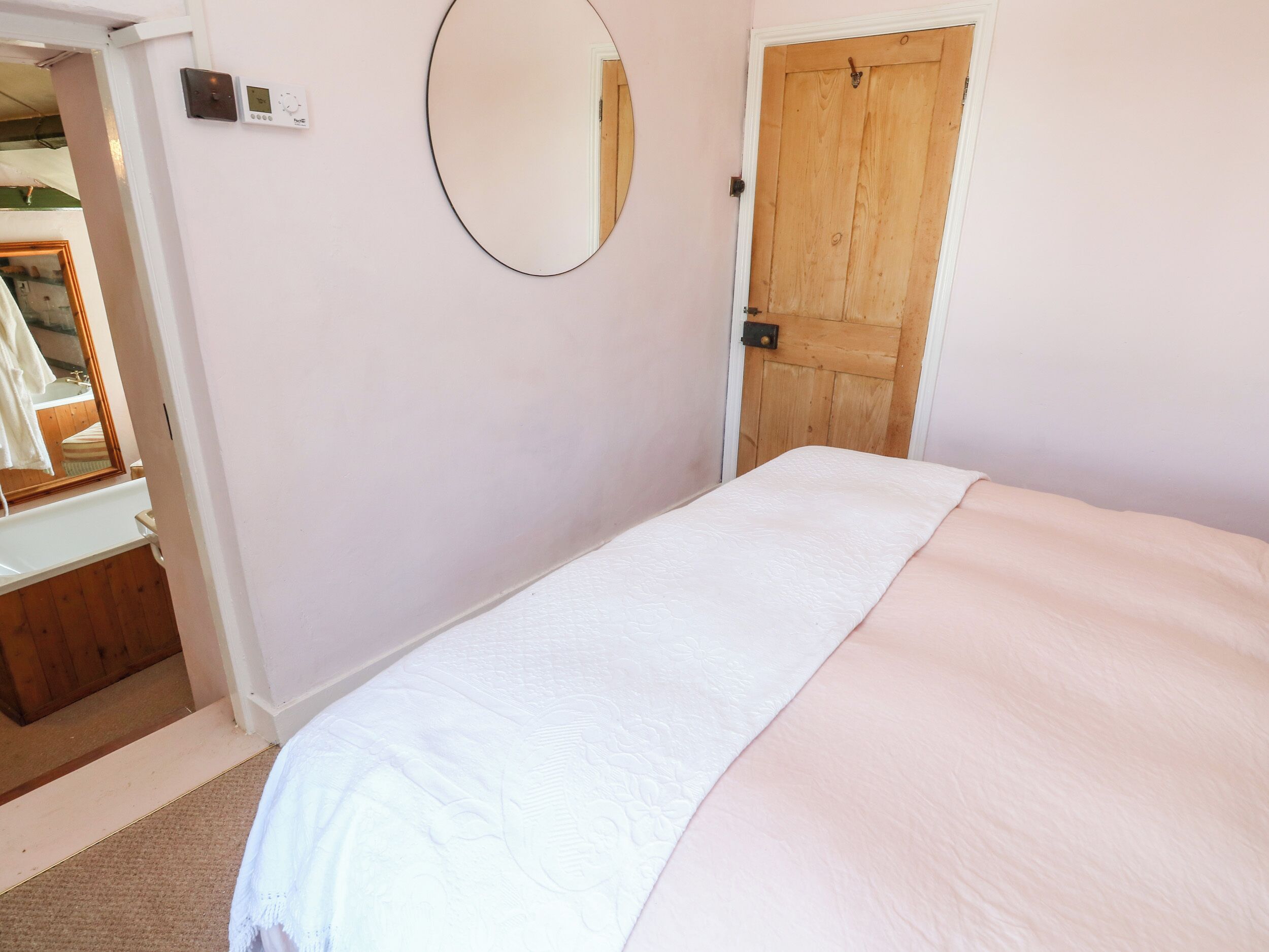 Un dormitorio con cama, una puerta de madera, un espejo y un termostato en la pared.