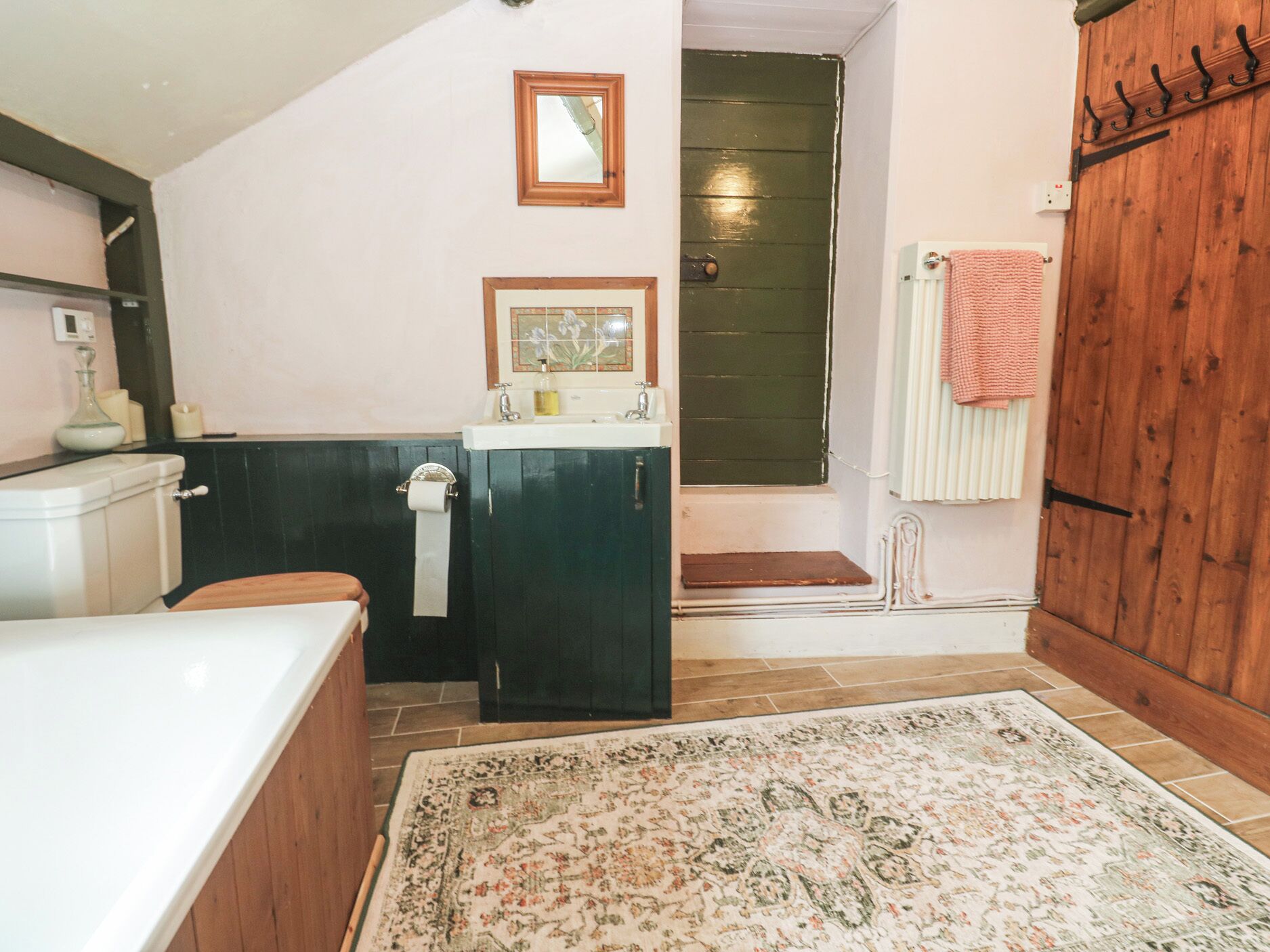 Une salle de bain avec une baignoire, un lavabo, des toilettes, une porte en bois et un tapis à motifs.