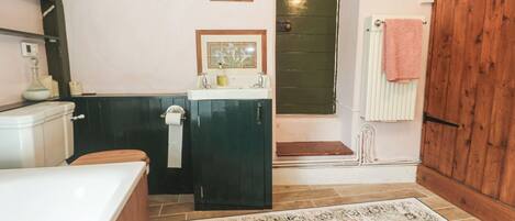 Une salle de bain avec une baignoire, un lavabo, des toilettes, une porte en bois et un tapis à motifs.