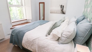 A bedroom with a bed, a window, a mirror, and a wall-mounted artwork.