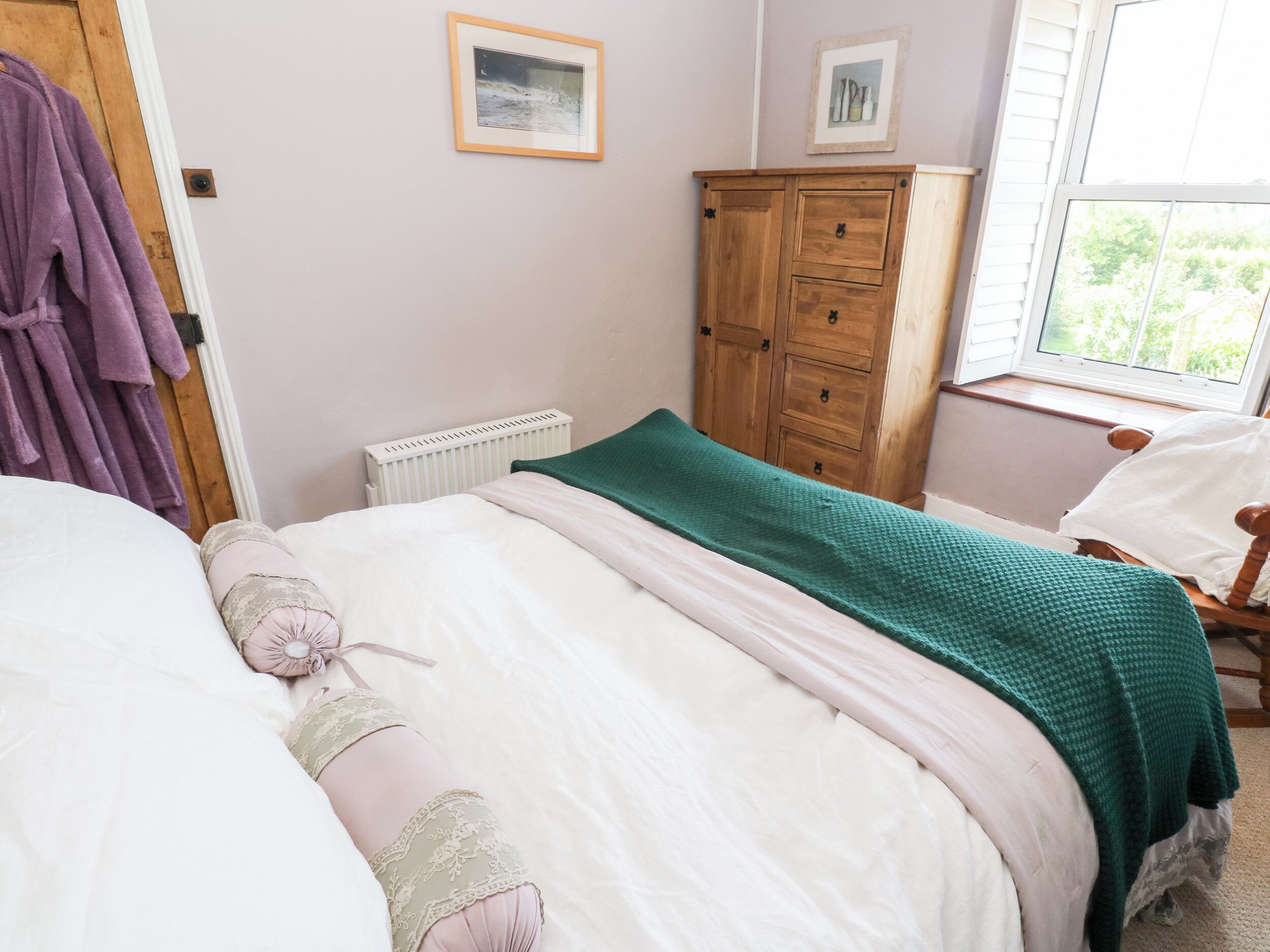Une chambre à coucher comprenant un lit, une armoire en bois, un radiateur et une fenêtre donnant sur un paysage verdoyant.