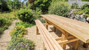 A wooden picnic table in a garden with gravel paths and various plants.
