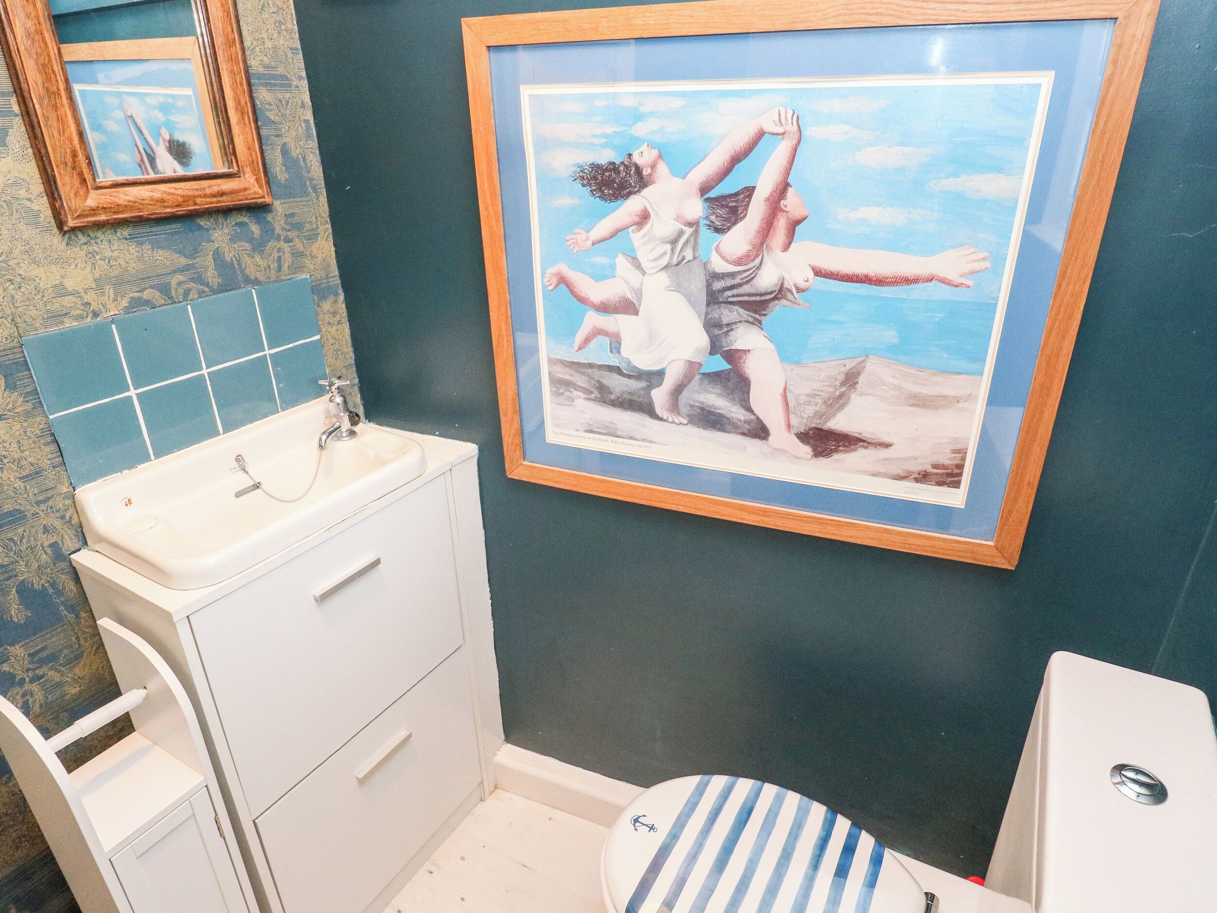 A bathroom with a sink, toilet, and a framed painting of people dancing.