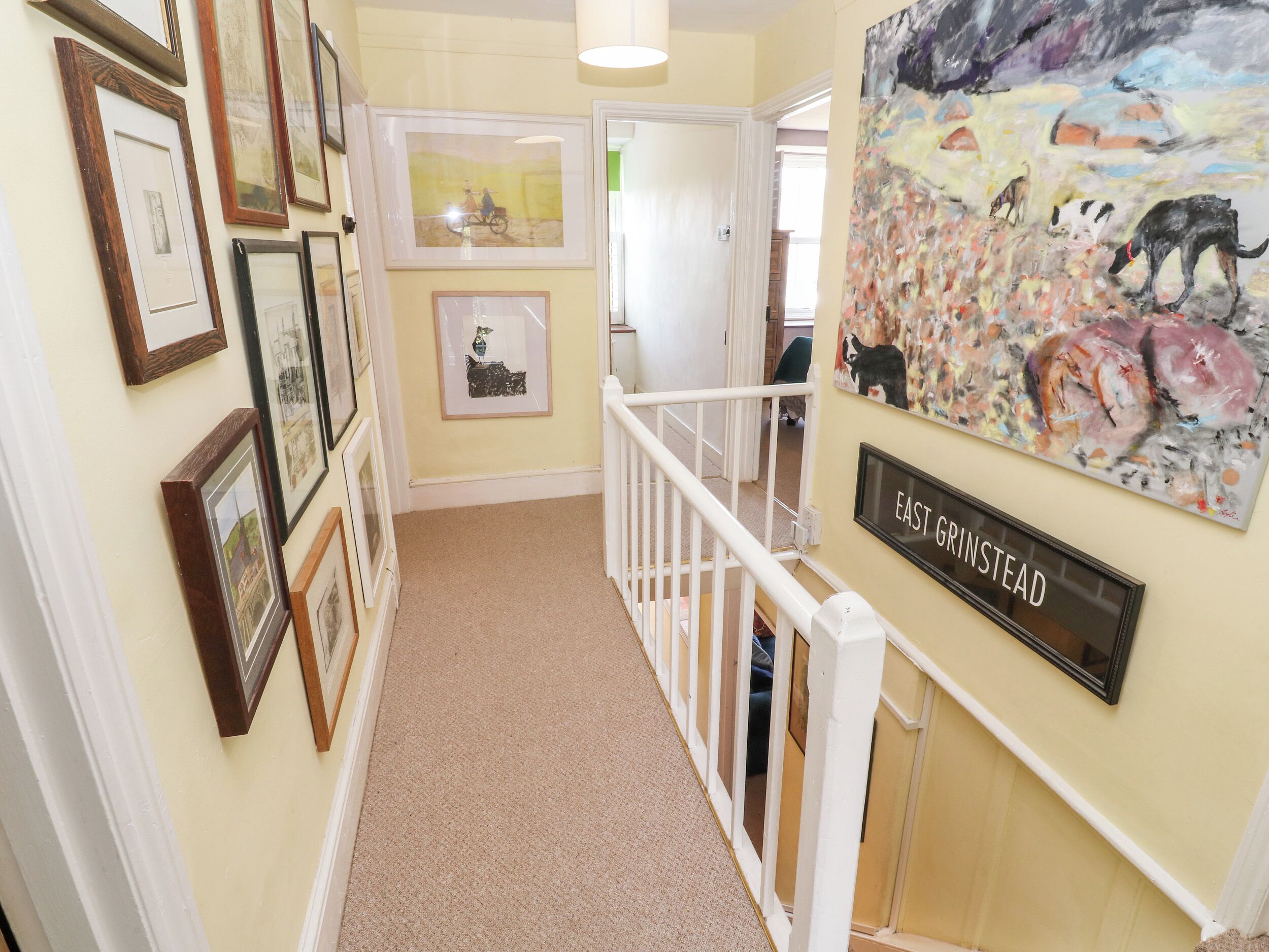 A hallway with framed pictures on the walls, a white railing, and a sign that reads "EAST GRINSTEAD".