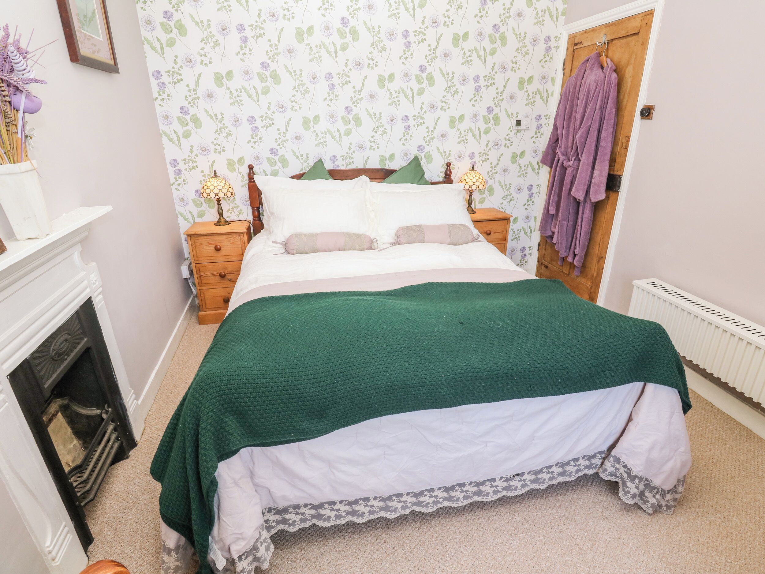 A bedroom with a bed, two bedside tables, a dresser, a fireplace, and a door.