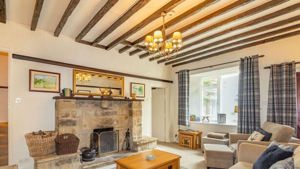 A cozy living room with a stone fireplace, wooden beams, a sofa, and a window with curtains. - Clifford House Farm (Skipton)