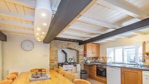 A kitchen with a stone arch, wooden cabinets, a built-in oven, and a dining area with a wooden table and chairs. - Clifford House Farm (Skipton)