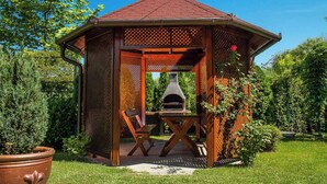 A wooden gazebo with a chimney, two wooden chairs, and a table in a garden. - Holiday apartment with pool and well-kept garden, air conditioning, safe (Balatonmáriafürdő)