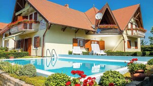 A hotel with a swimming pool, balconies with flower boxes, and a clear blue sky. - Holiday apartment with pool and well-kept garden, air conditioning, safe (Balatonmáriafürdő)