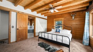 Une chambre avec un plafond en bois, un lit, un ventilateur de plafond et une décoration représentant une tête de cerf.