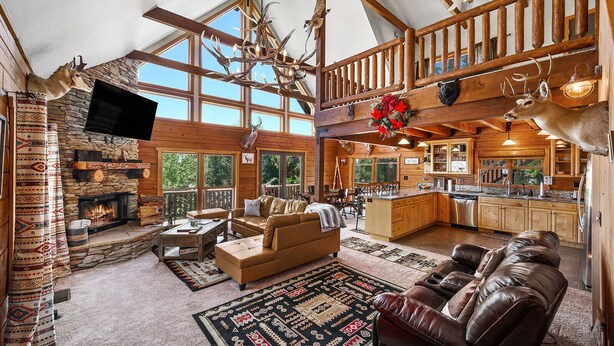Un chalet spacieux doté d’une cheminée en pierre, de meubles en cuir, d’une cuisine et d’un balcon avec des balustrades en bois.